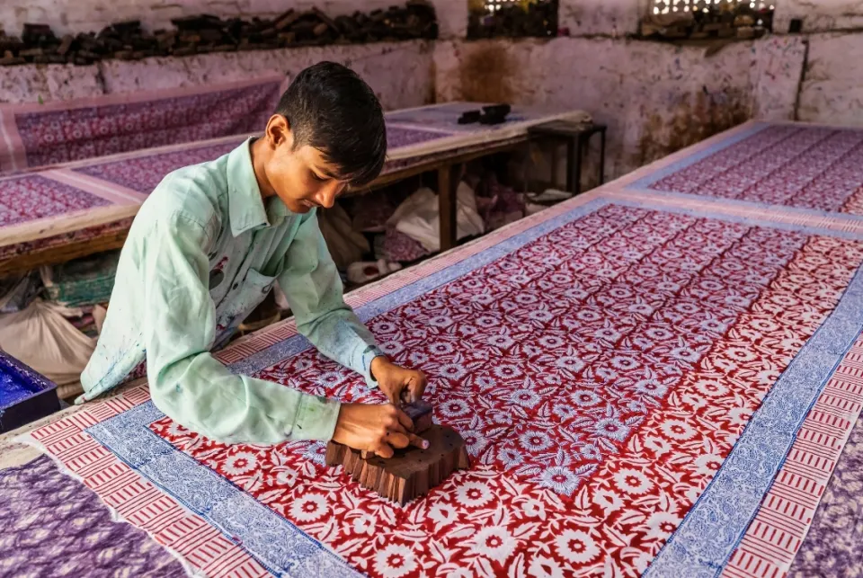 Artisan hand-printing patterned fabric using a carved wooden block in a traditional Rajasthan textile workshop.