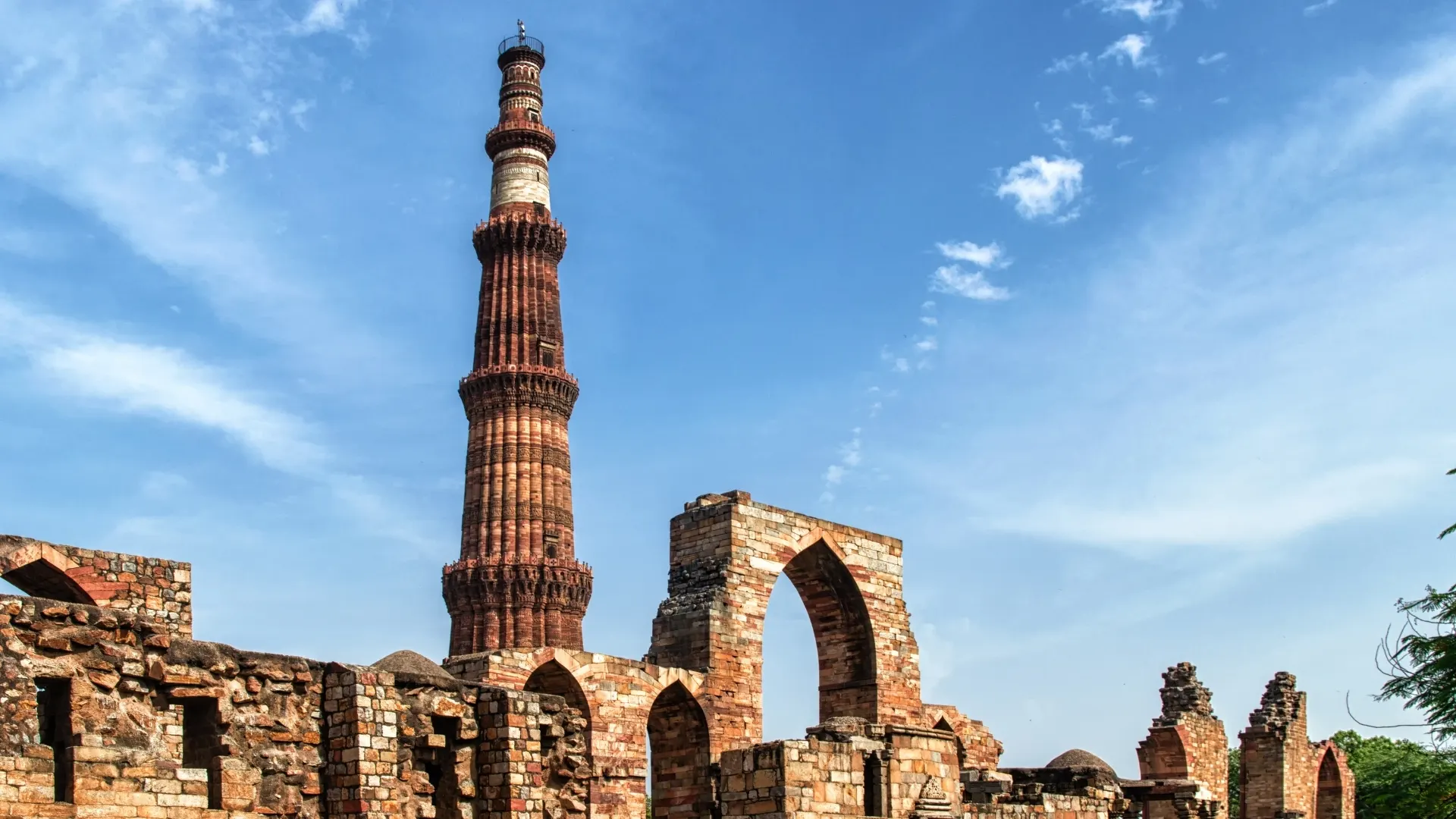 Qutub Minar rising above stone ruins and arched gateways in Delhi