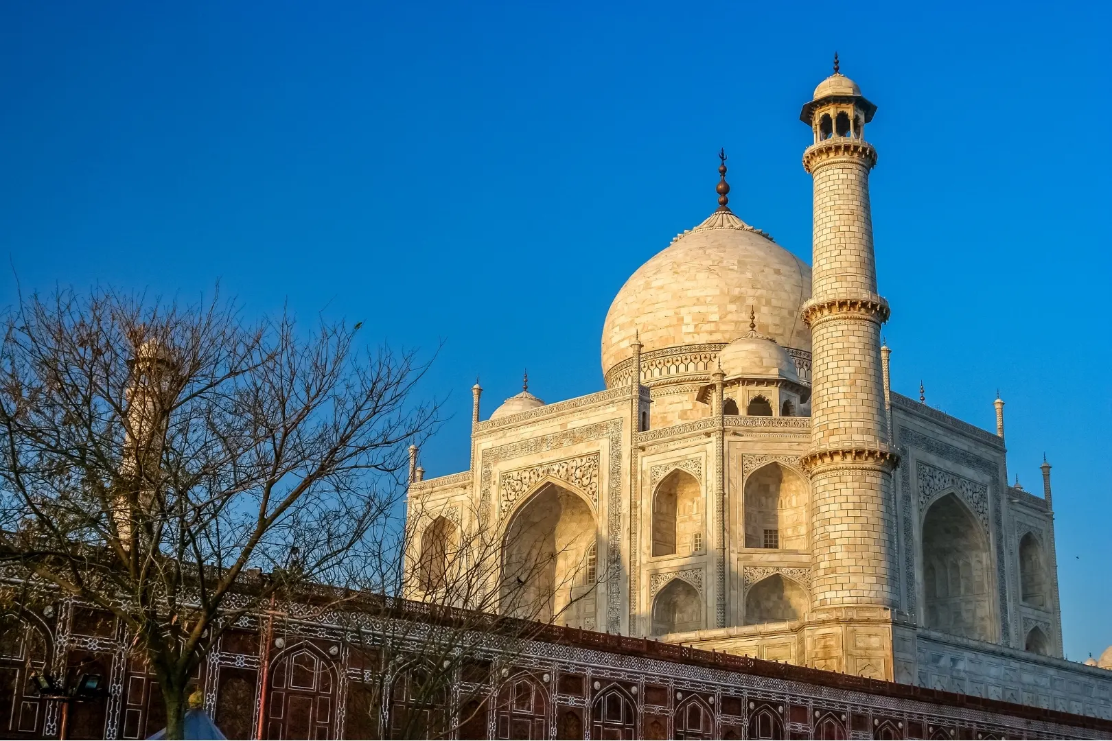 Side view of the Taj Mahal with a marble minaret against a clear blue sky