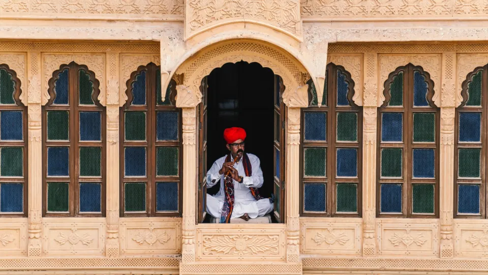 Rajasthani folk musician sitting in stone window with traditional instrument