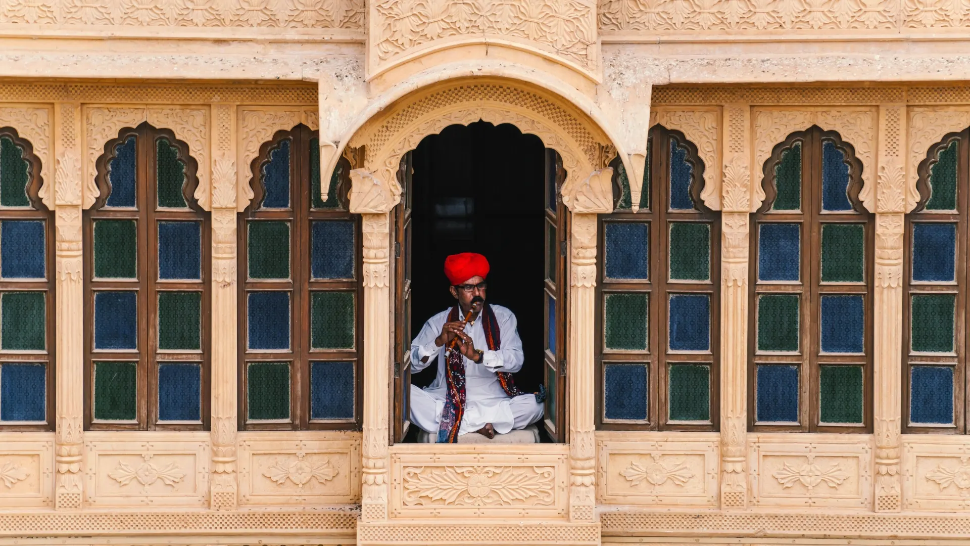 Rajasthani folk musician sitting in stone window with traditional instrument