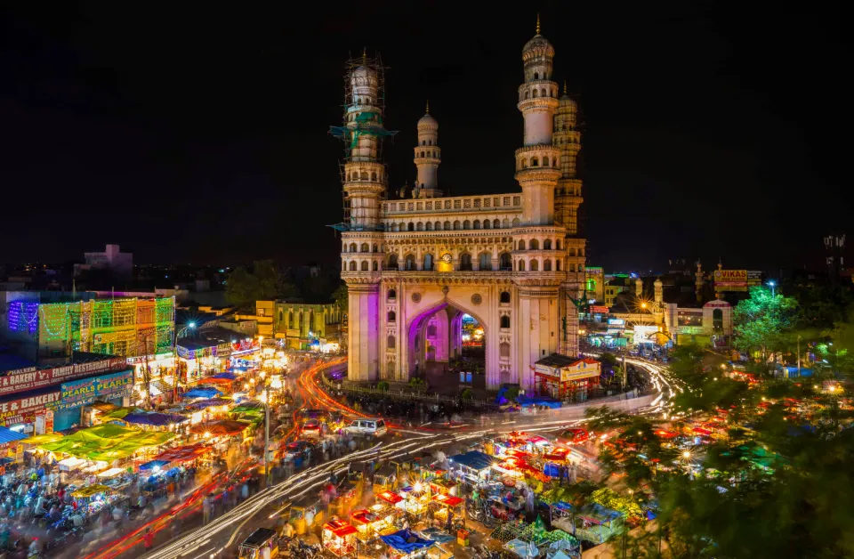 Charminar illuminated at night with colorful market lights and long-exposure traffic trails below