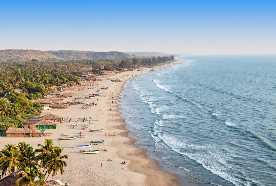 long sandy beach with fishing boats and shoreline activity in Goa