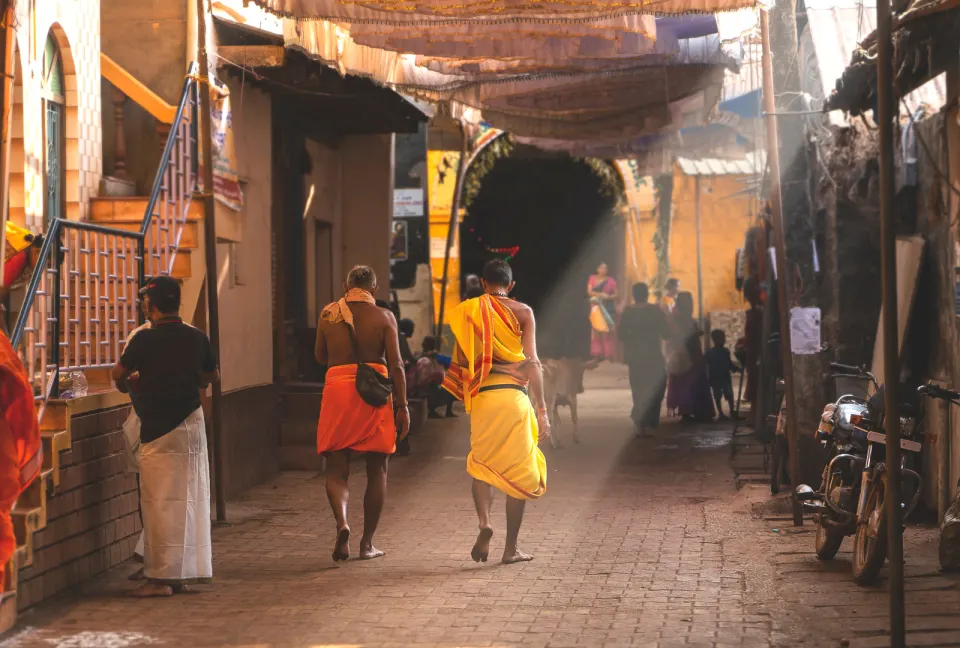 barefoot pilgrims walking through a temple street in Gokarna under fabric canopies