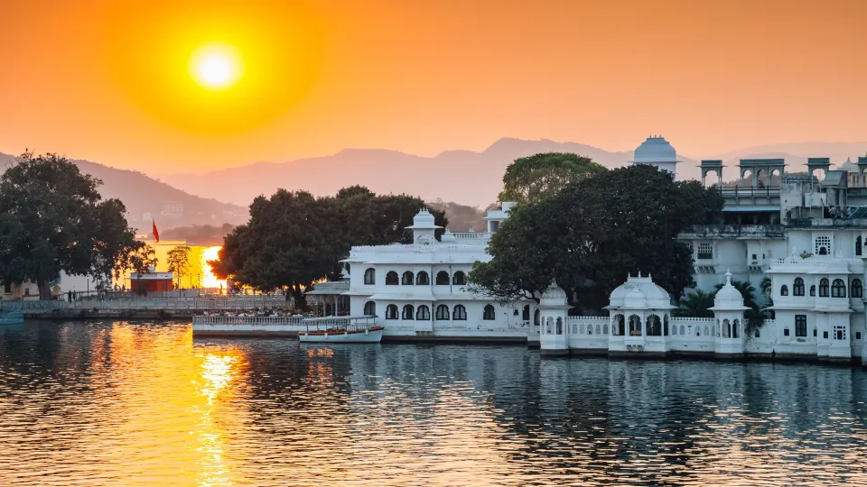 White palace complex reflected in Lake Pichola at sunrise