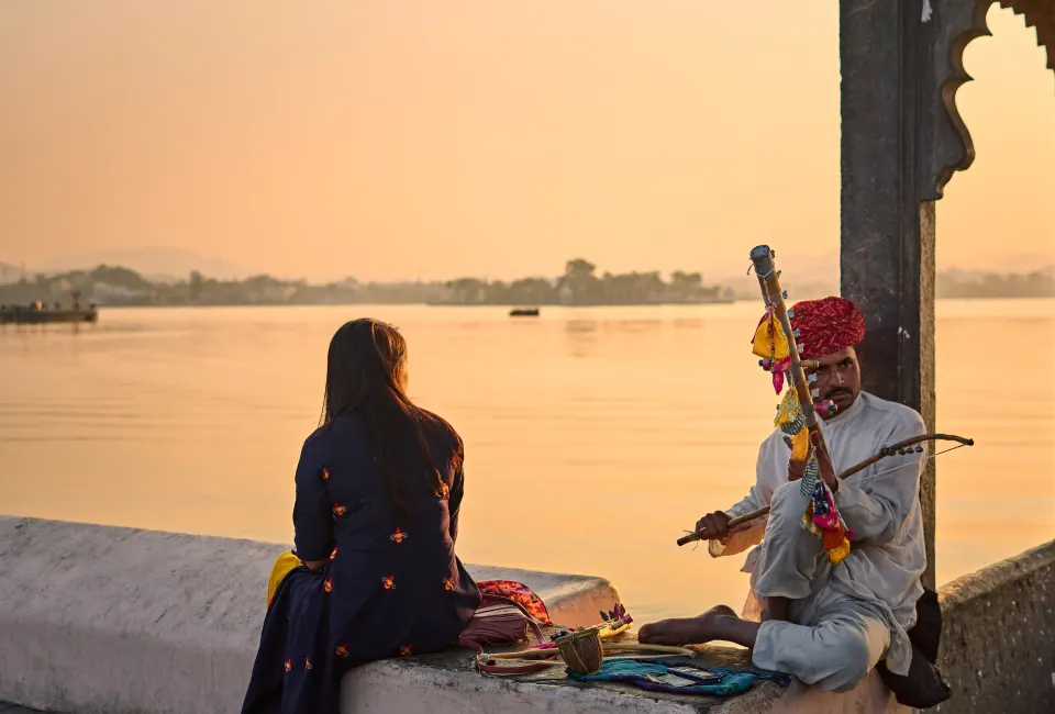 Local musician playing traditional instrument by Lake Pichola at sunset