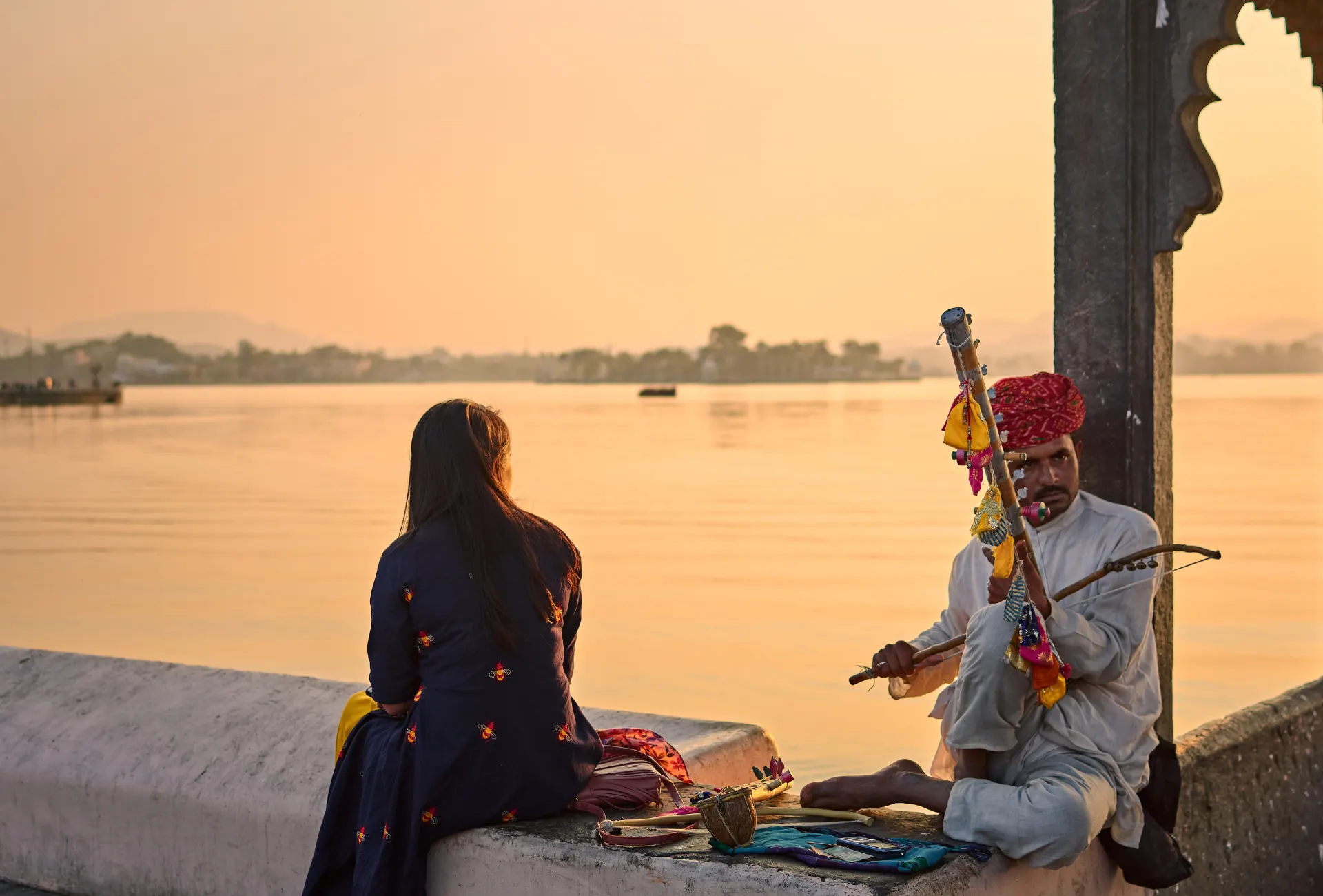 Local musician playing traditional instrument by Lake Pichola at sunset