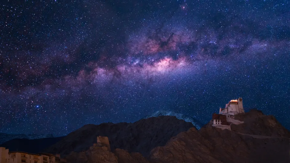 A remote Ladakhi monastery perched on a rocky outcrop, bathed in warm evening light against stark, shadowed mountain slopes