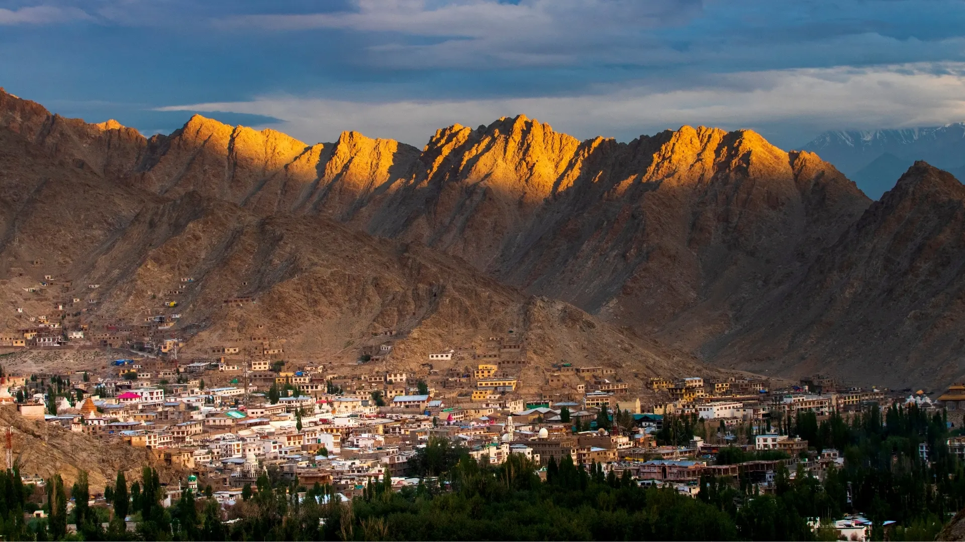 Leh town spread below sunlit mountain ridges at sunset
