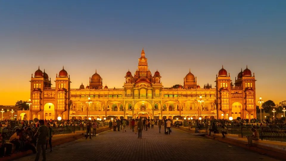 illuminated facade of mysore palace with visitors in the front courtyard at dusk
