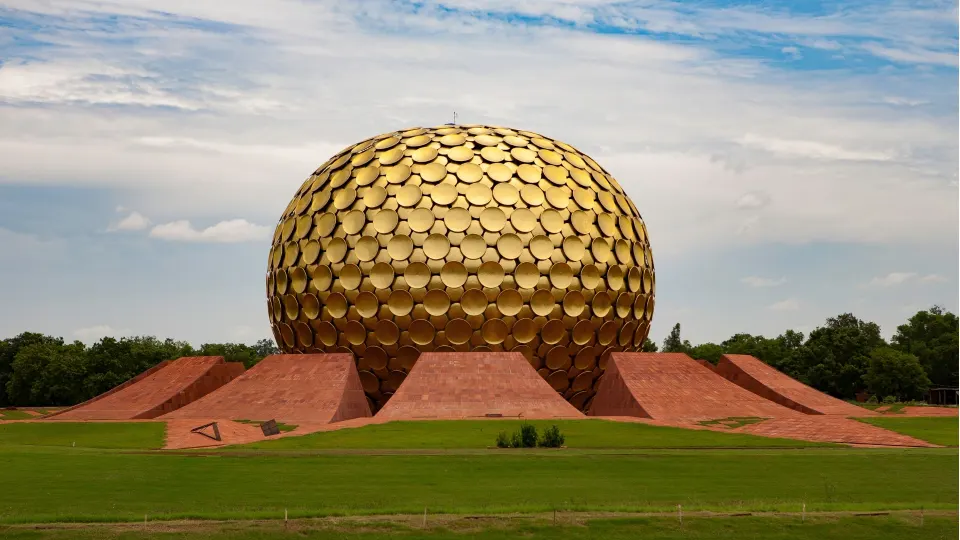 The golden Matrimandir dome in Auroville surrounded by green lawns under a partly cloudy sky
