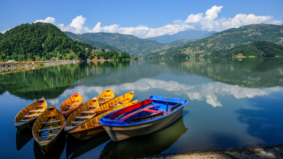 Colorful wooden boats resting on the calm waters of Phewa Lake with mountains and clouds reflected clearly