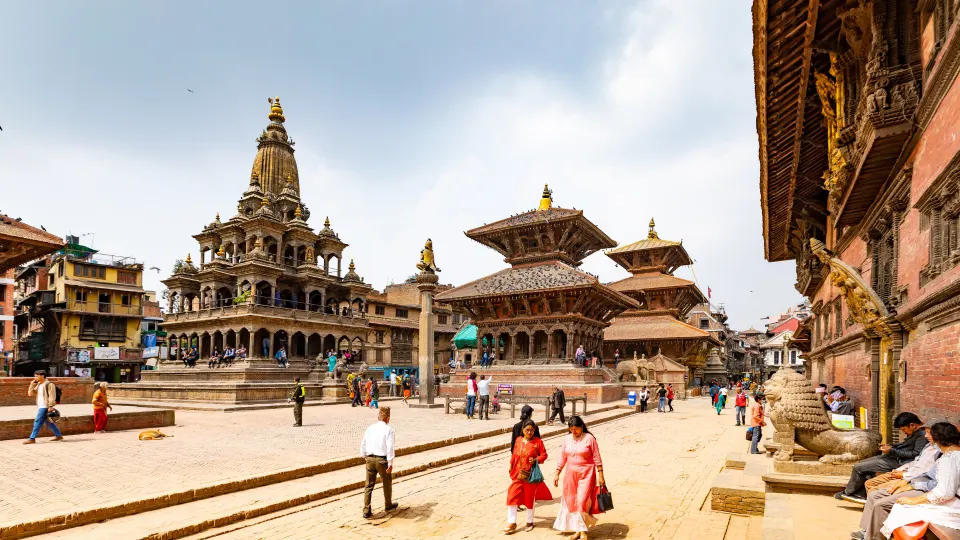 Historic temples and stone structures in Patan Durbar Square with people walking across the plaza