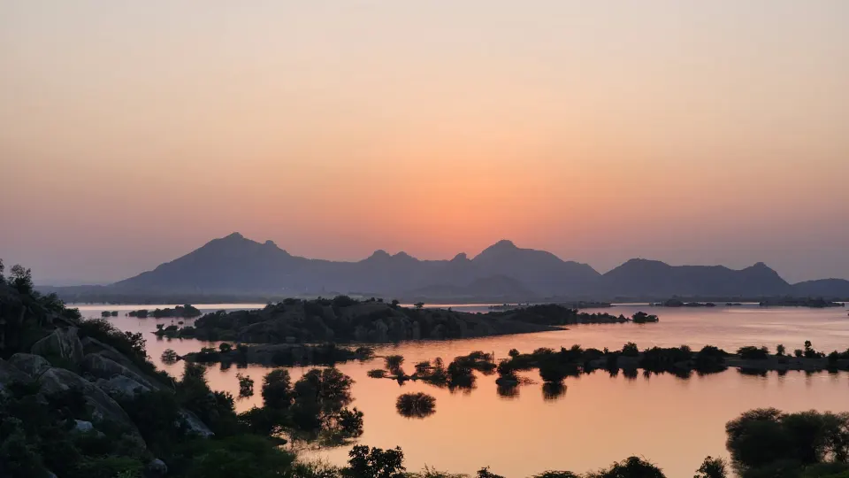 A wide lake reflecting mountains during a soft orange sunset