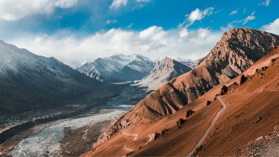 A wide Himalayan valley with rugged brown slopes, snow peaks in the distance, and a winding riverbed