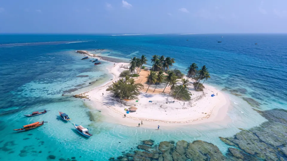 Aerial view of a small Lakshadweep sandbank island with palm trees surrounded by turquoise water