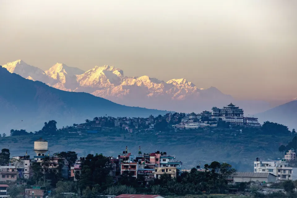 Snow-covered Himalayan peaks rising behind a hilltop monastery and valley settlement