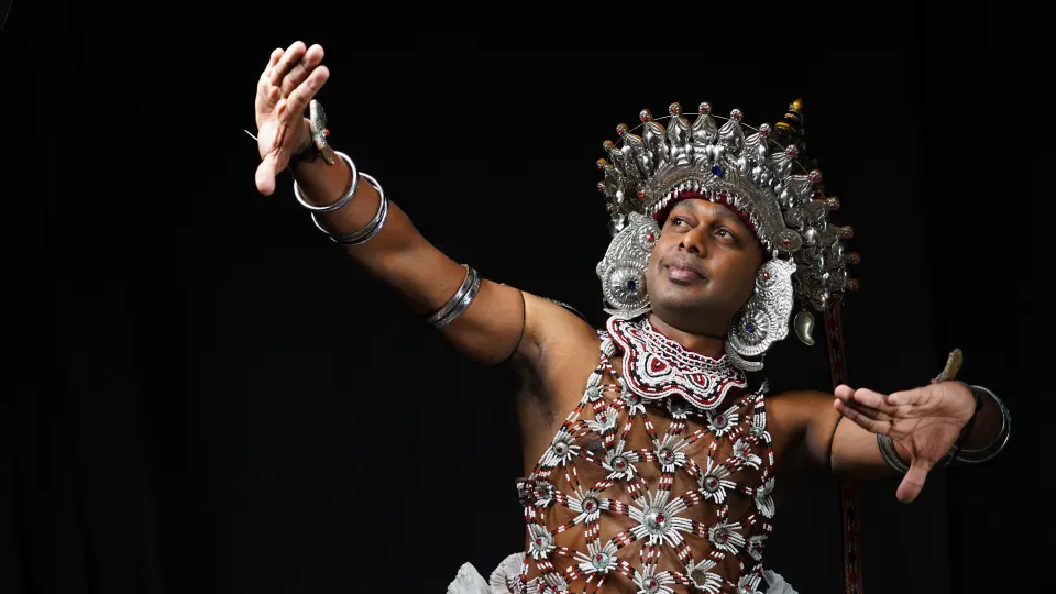Kandyan dancer in ornate silver headpiece performing against a black stage backdrop