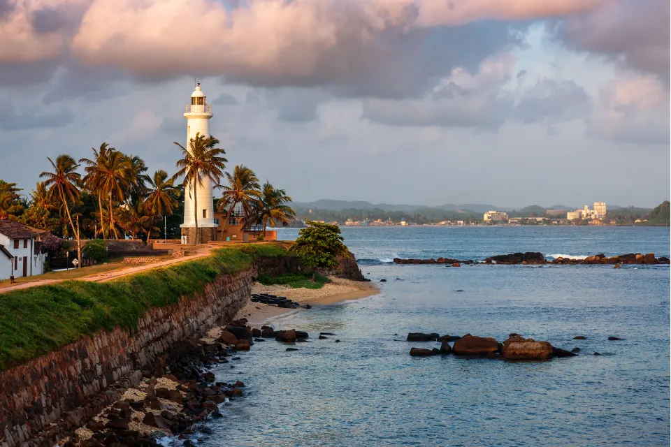 Galle Fort Lighthouse beside the sea with palm trees and evening clouds