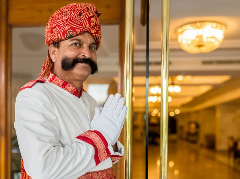 Rajasthani hotel doorman in traditional attire welcoming guests at a luxury palace hotel entrance.